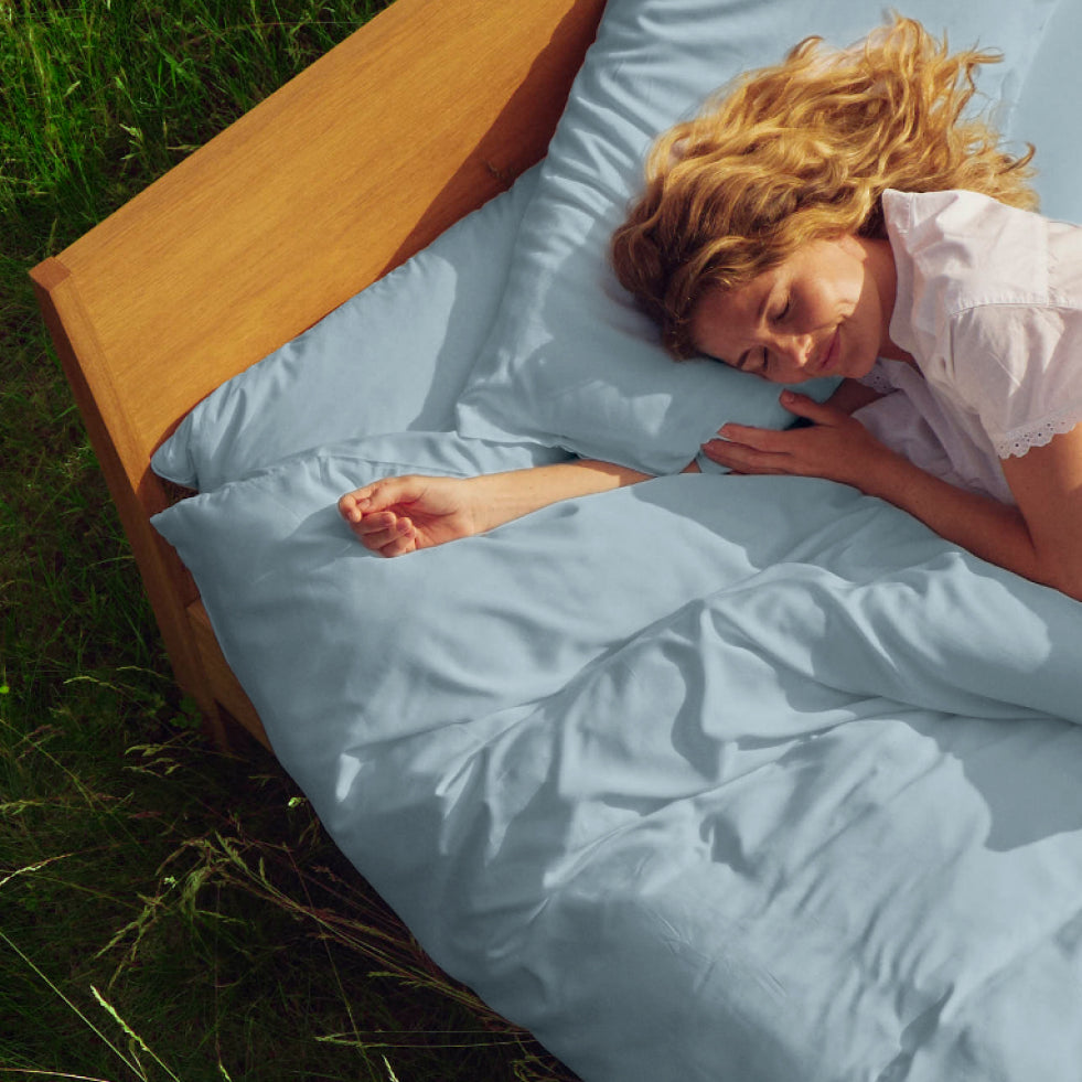 A woman lies on her side on a bed with blue spruce bedding and matching pillows