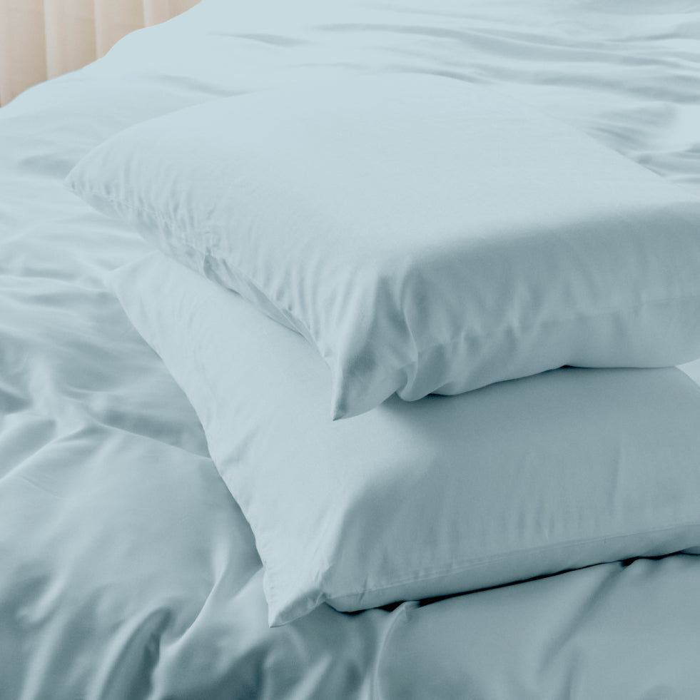 Two bamboo blue spruce pillows stacked on a matching bedsheet duvet