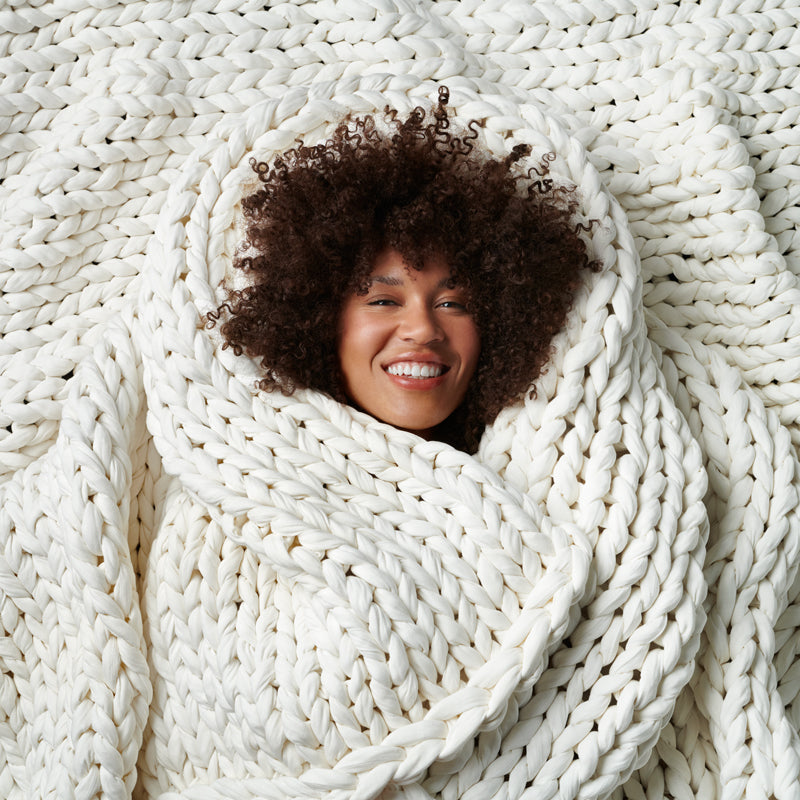 Happy woman about to fall asleep faster under the AURTRS weighted blanket