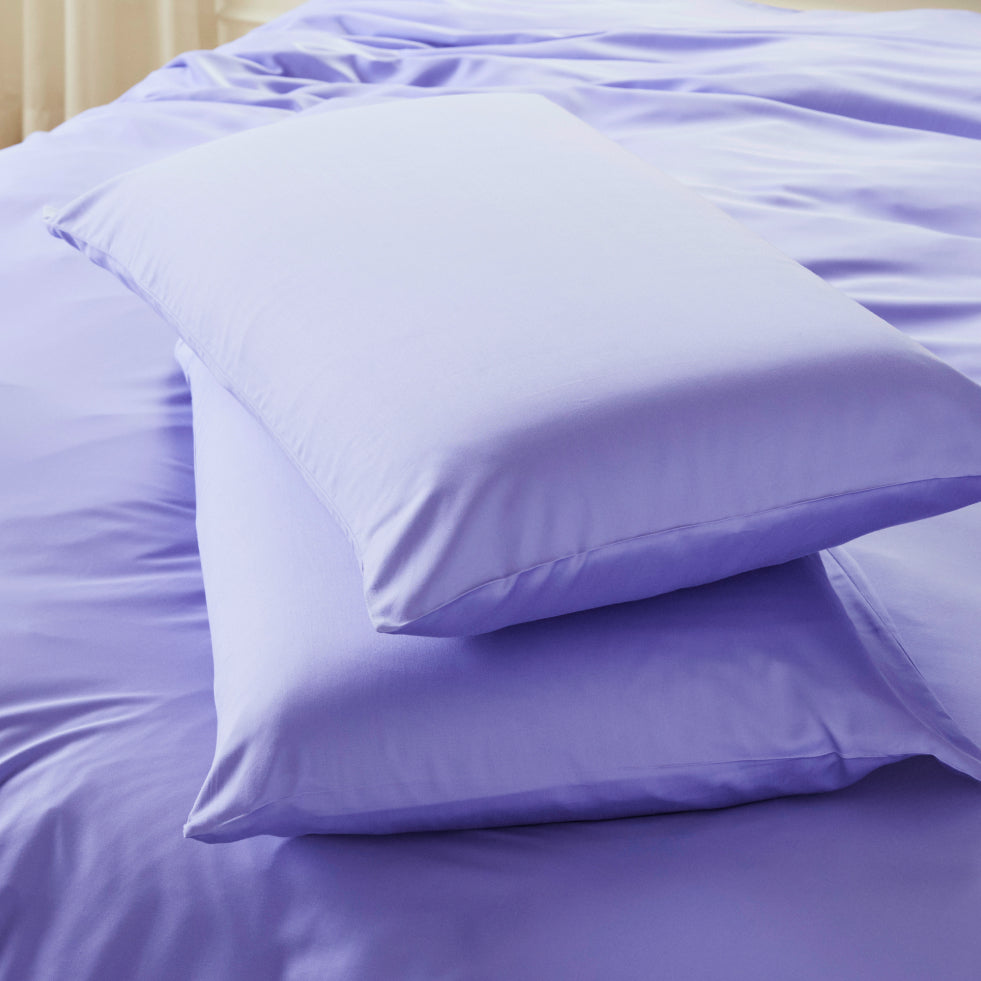 Two lavender-colored AURTRS pillowcase stacked on top of matching lavender bedding