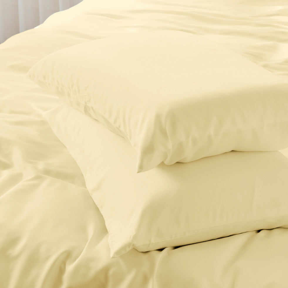A close-up of lemon icing bedding with two stacked pillows and matching duvet or sheet on a bed.