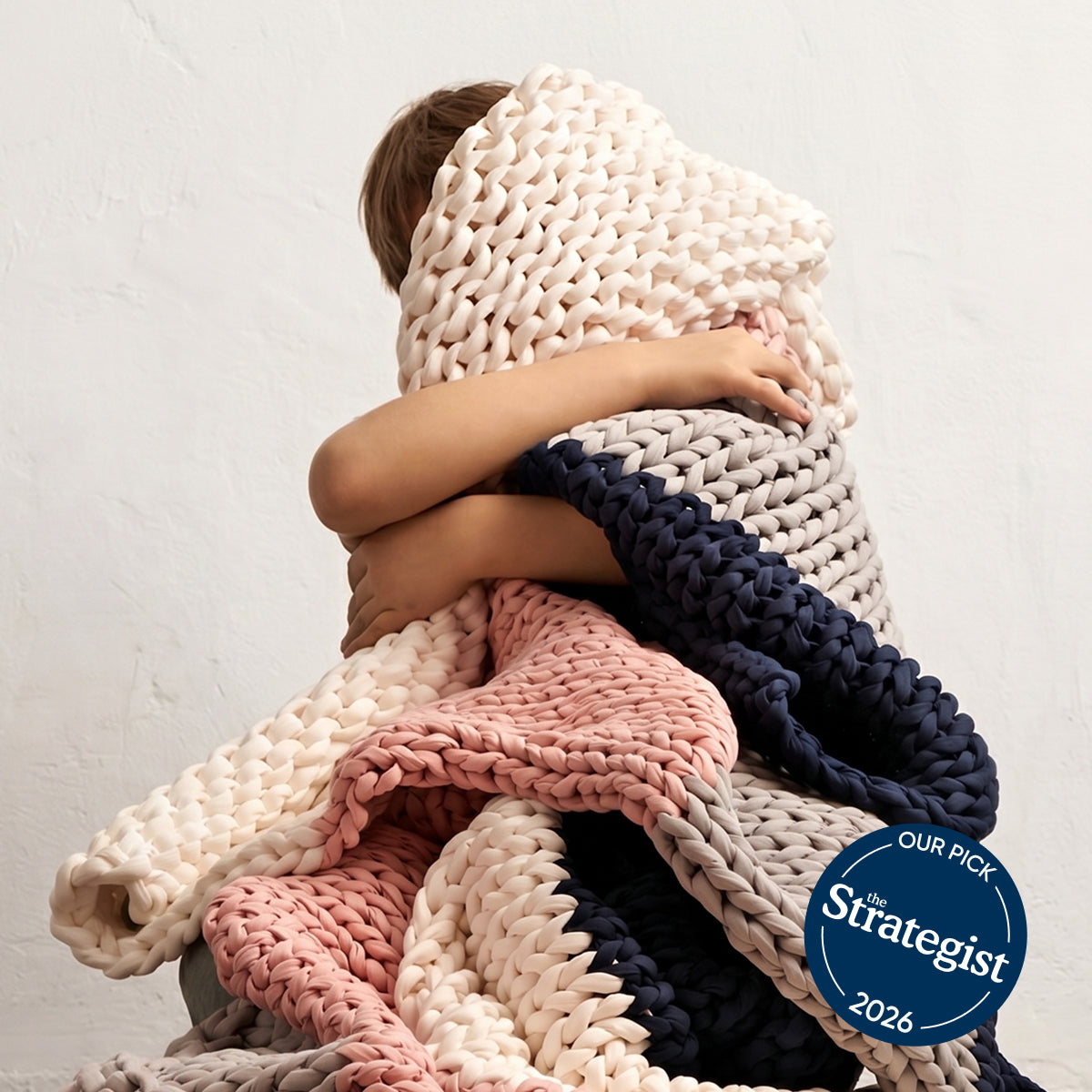 Children wrapped in a AURTRS chunky knit kids blanket with 'The Strategist' 2026 pick badge.